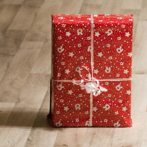 A beautifully wrapped gift box with red paper and white ribbon on a wooden floor.